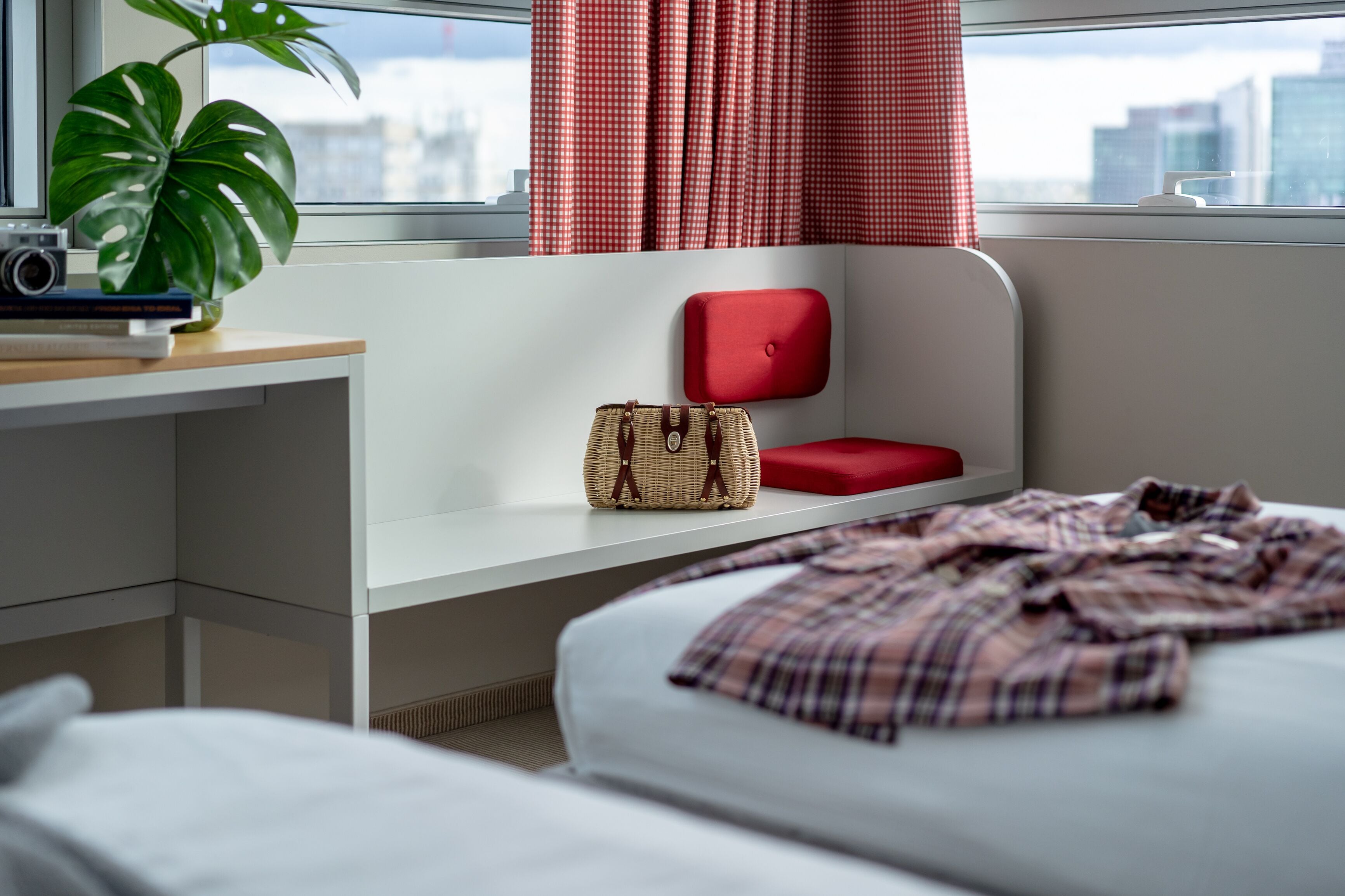 Ein modernes Hotelzimmer mit einem Bett, einem Schreibtisch mit Kamera, einer Pflanze und einem roten Sessel.
