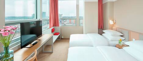 A hotel room with a bed, a desk with a TV, a chair, and a window with a view of the city.