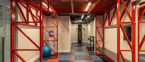 A gym with red metal frames, exercise equipment, a blue exercise ball, and an orange mat.