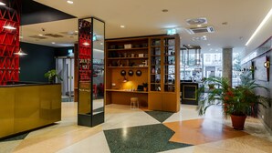 Un moderno vestíbulo de hotel con una mesa de recepción, una zona de estar con una computadora portátil y una estantería con diversos objetos.