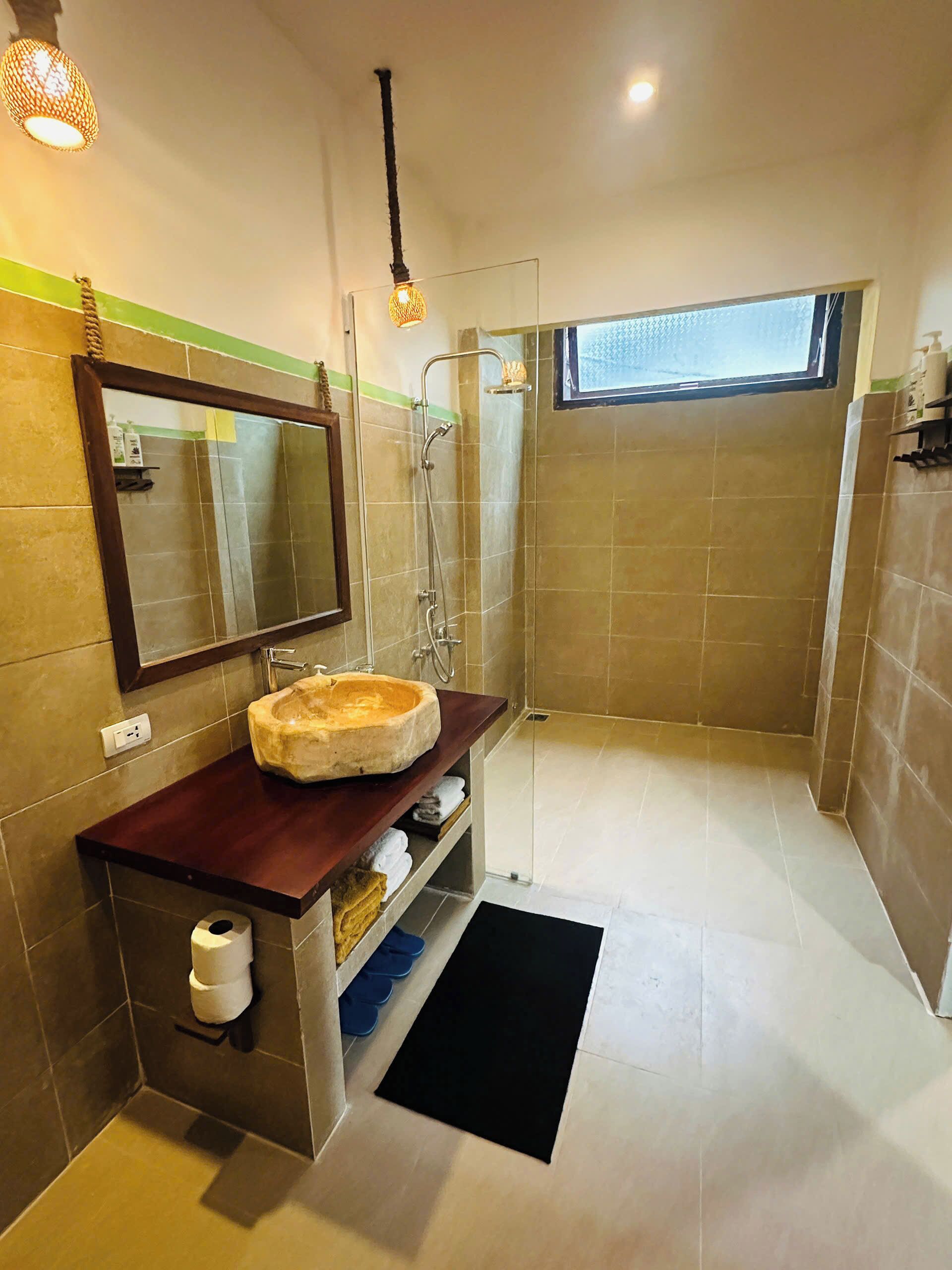 Un baño moderno con un espejo grande, un lavabo redondo, una ducha y un ventanal pequeño.