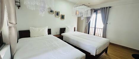 A hotel room with two beds, a wooden floor, a ceiling fan, and a window with curtains.