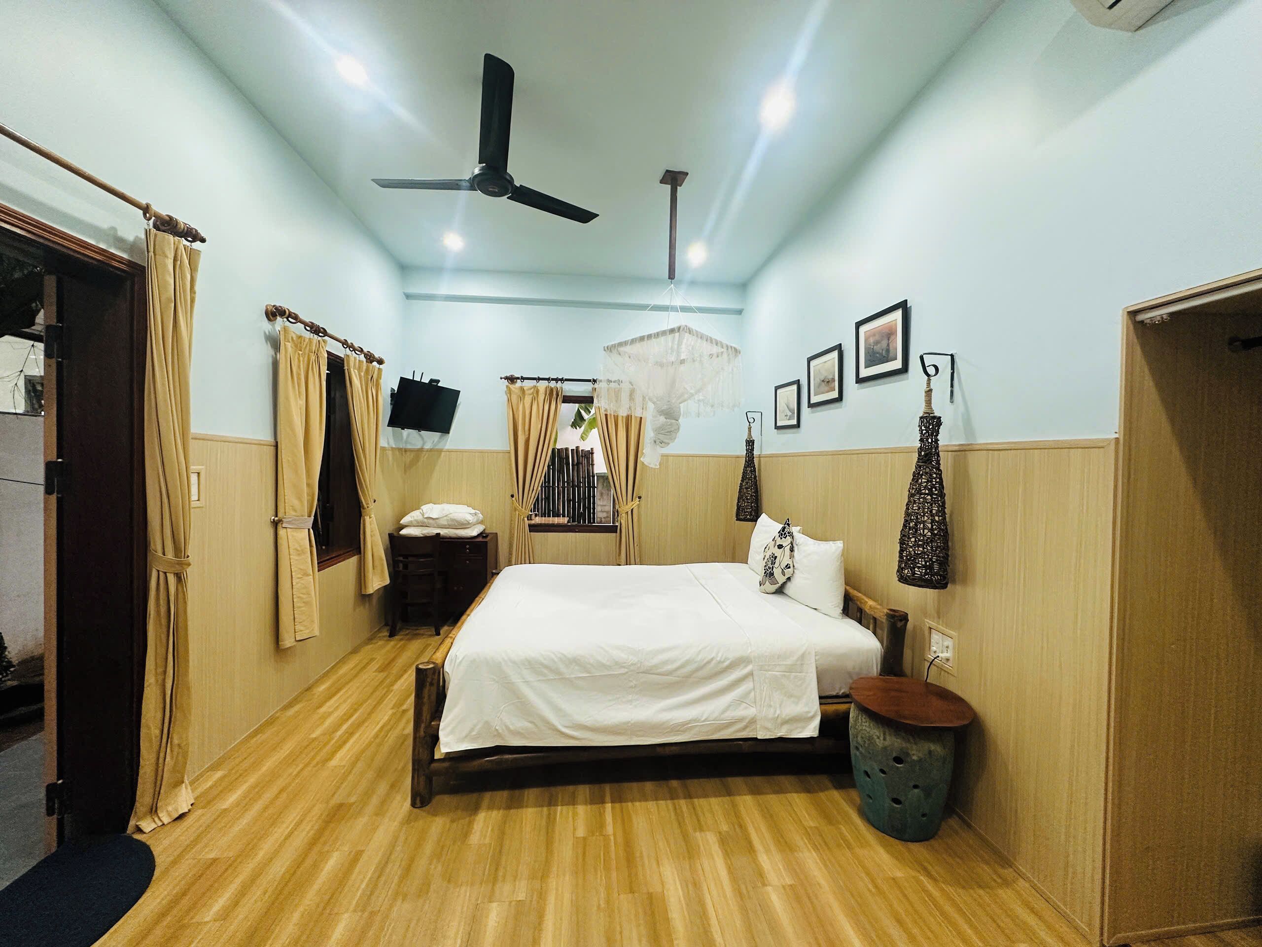 A bedroom with a bed, a ceiling fan, a bedside table, a nightstand, a window with curtains, and wall-mounted lights.