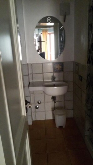 A bathroom with a white sink, a mirror, and a trash bin. - Hotel Bella Napoli (Agrigento)