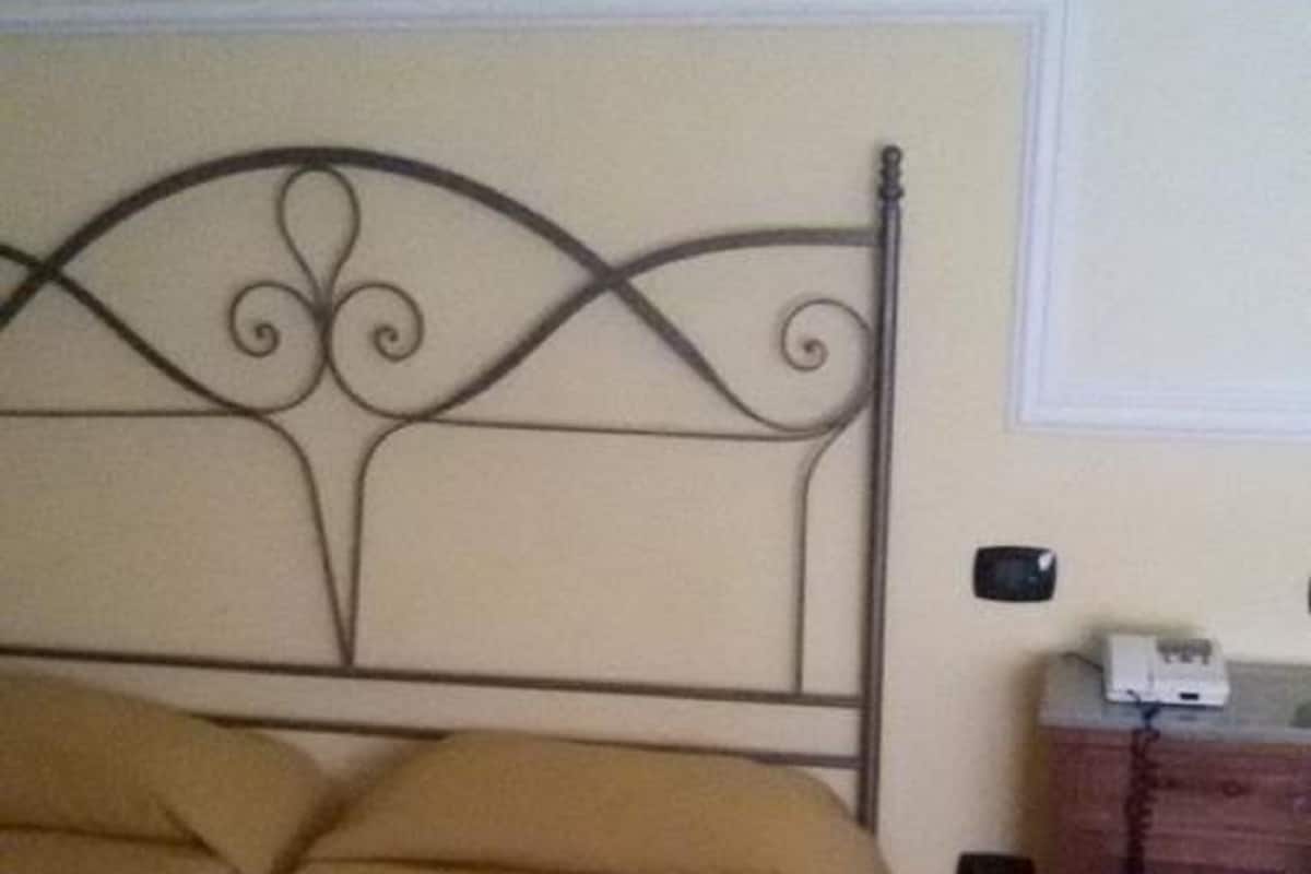 A bed with a metal headboard, a wooden nightstand with a telephone, and a tiled floor.