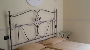 A room with a metal bed frame, a round wall decoration, and a small table. - Hotel Bella Napoli (Agrigento)
