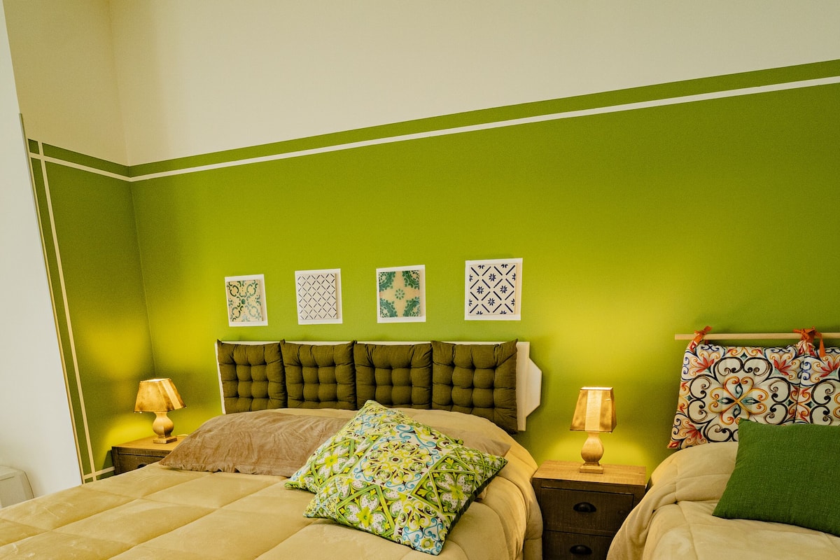 Une chambre avec deux lits, des murs verts et quatre tableaux encadrés accrochés au mur.