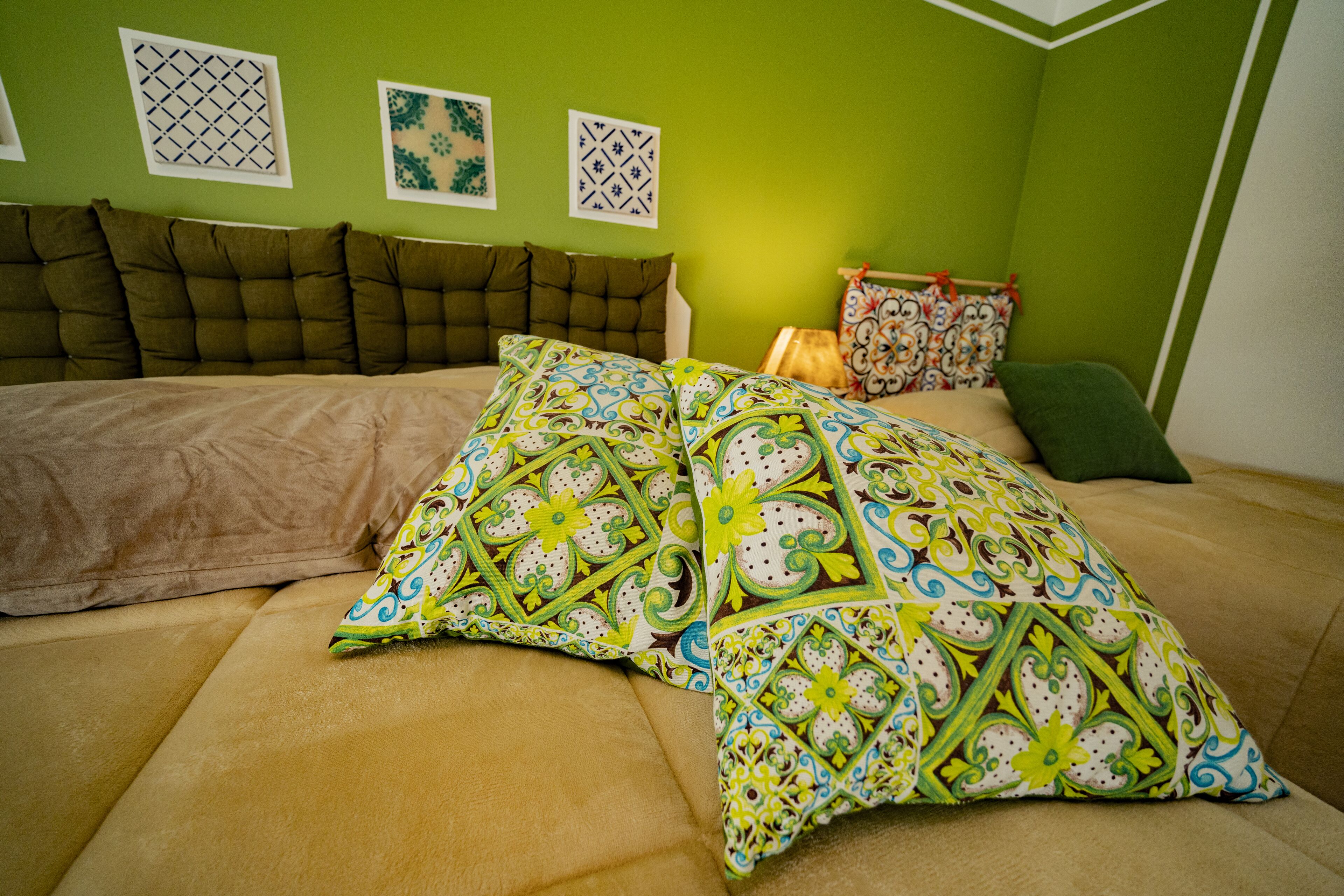 A bedroom with a bed, green walls, and patterned pillows.
