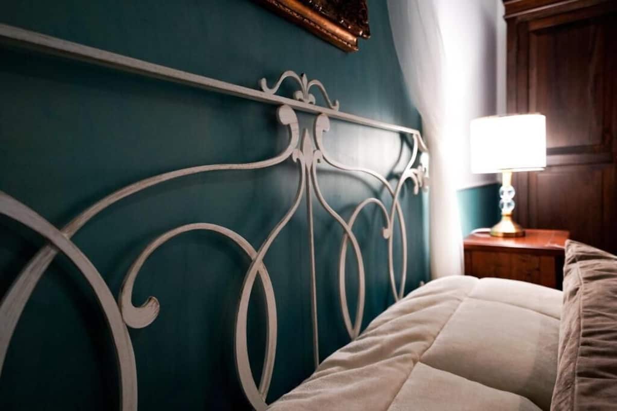 Un lit avec une tête de lit blanche, adossé à un mur de couleur turquoise, une table de chevet en bois avec une lampe, et une porte en bois en arrière-plan.