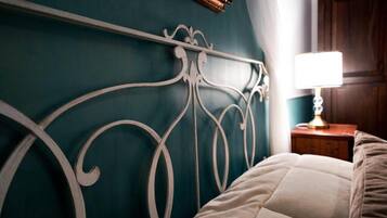 Un letto con testiera bianca su pareti color verde acqua, un comodino in legno con una lampada e una porta in legno sullo sfondo.