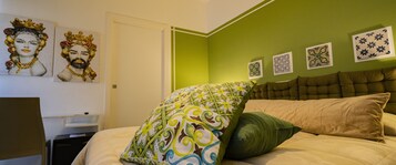 Quarto com parede verde, cama com almofadas estampadas e obras de arte na parede.