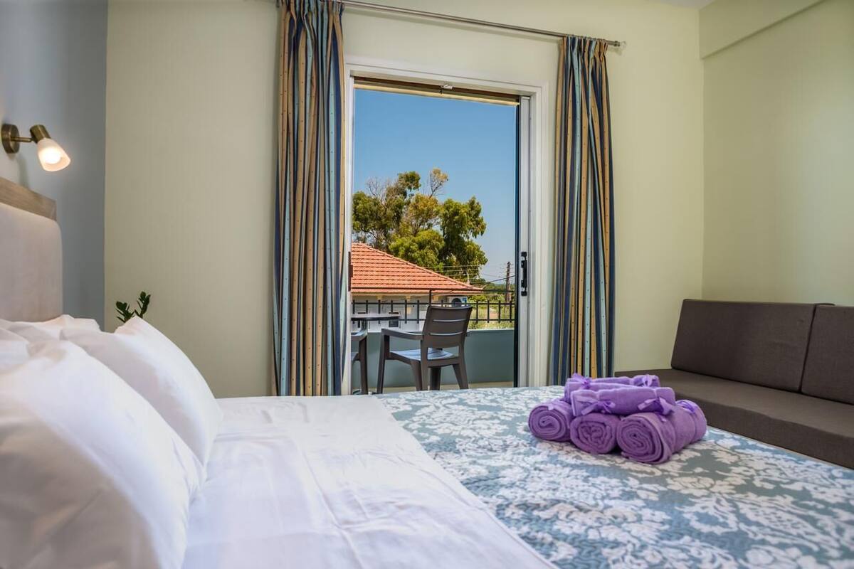 Habitación de hotel con cama, un pequeño balcón con mesa y sillas, y un sofá.