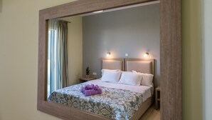 A hotel room with a large mirror, a bed with white linens, a small bedside table with a lamp, and a window with curtains. - Blue Lagoon (Zakynthos)