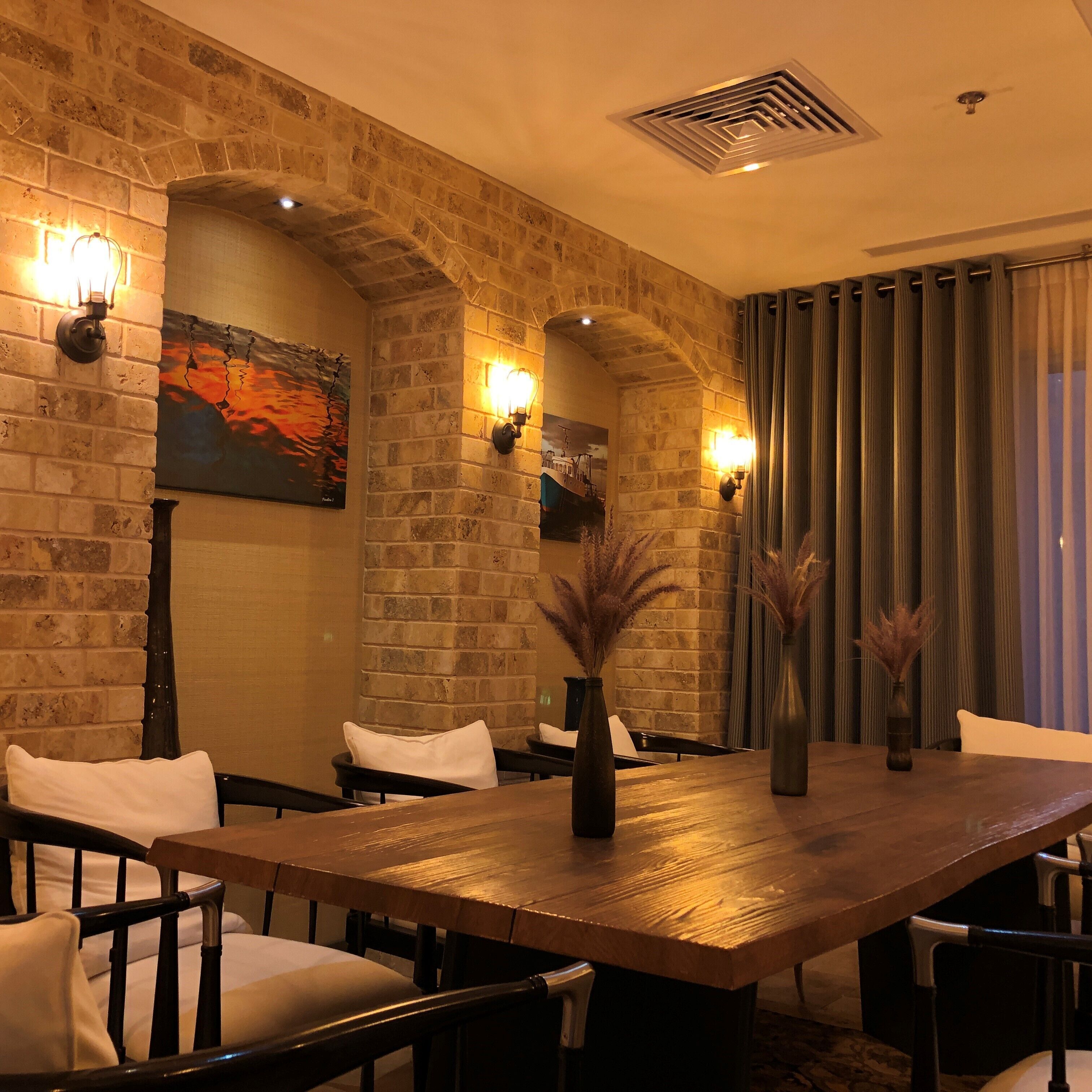 Un salón de conferencias con una larga mesa de madera, cuatro sillas, dos luminarias fijadas a la pared y un cuadro en la pared de ladrillo.