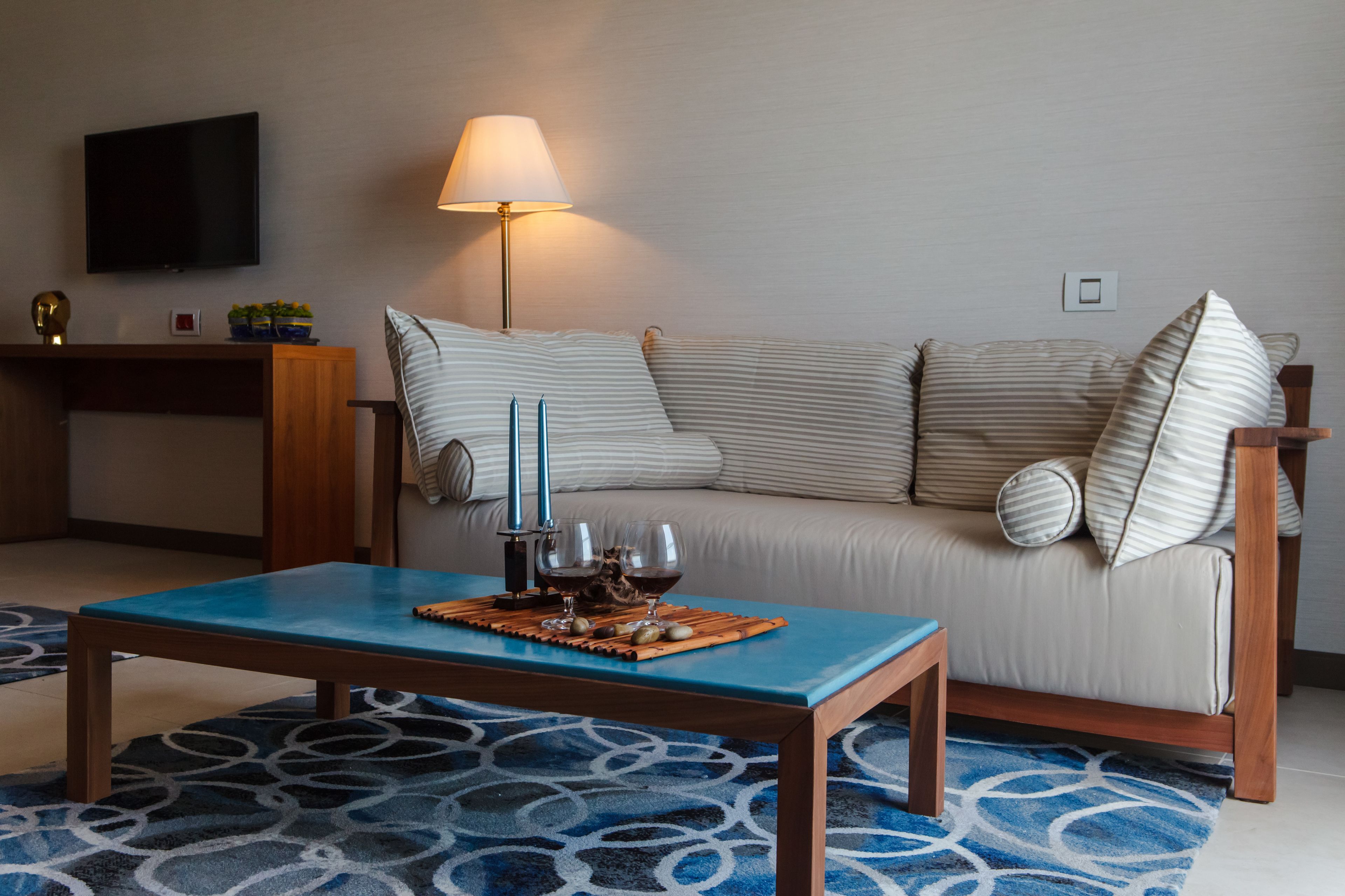 A living room with a sofa, a coffee table, a lamp, and a flat-screen TV on the wall.