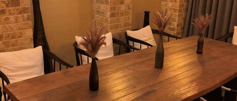 Une longue table en bois, ornée de deux vases contenant des plantes séchées, entourée de chaises dotées de coussins blancs.