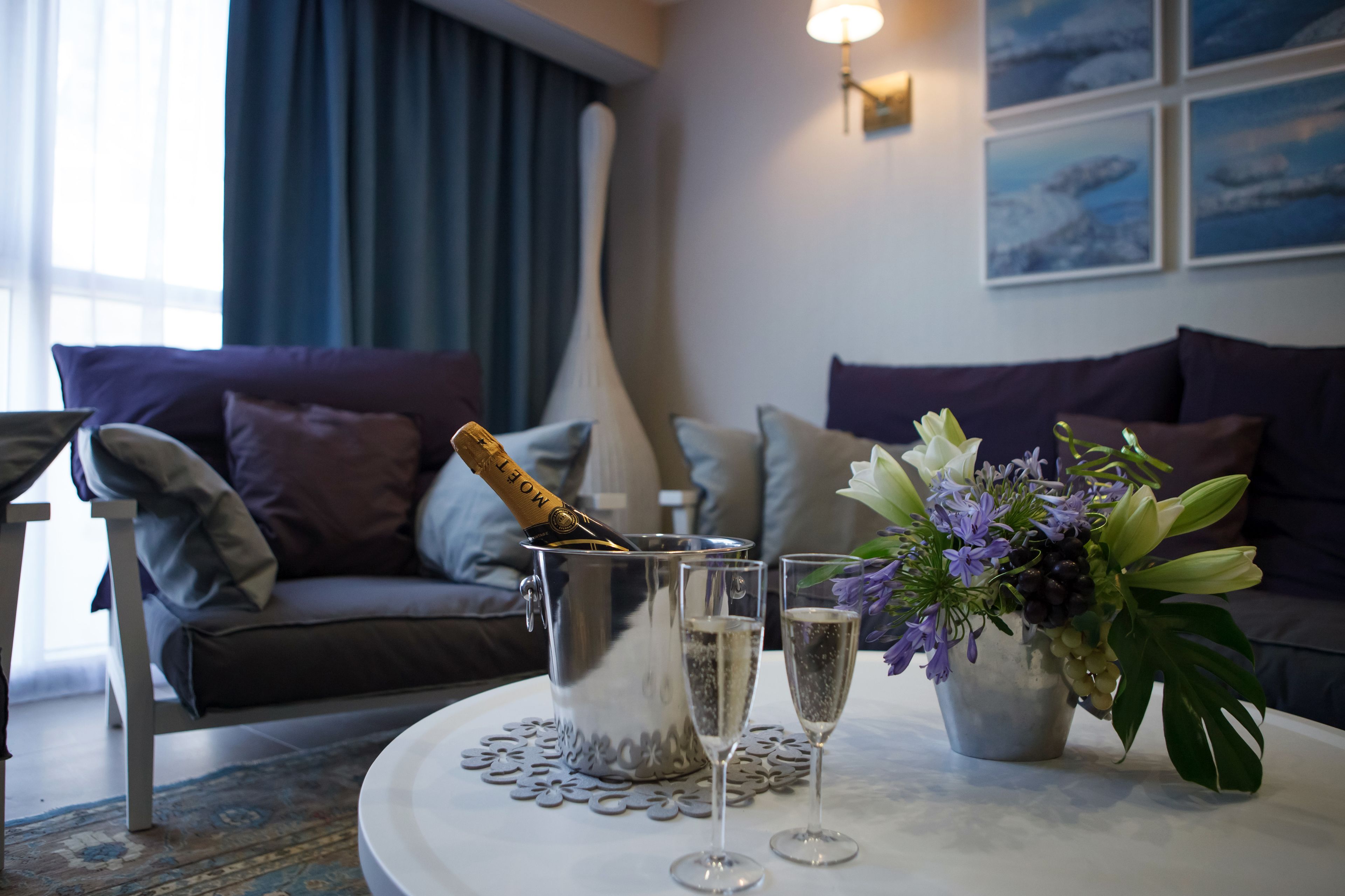 A room with a sofa, a table with a champagne bottle, glasses, and a flower arrangement.