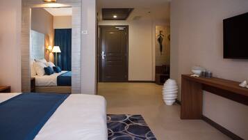 Habitación de hotel con cama, escritorio, televisión y baño visible a través de una puerta abierta.