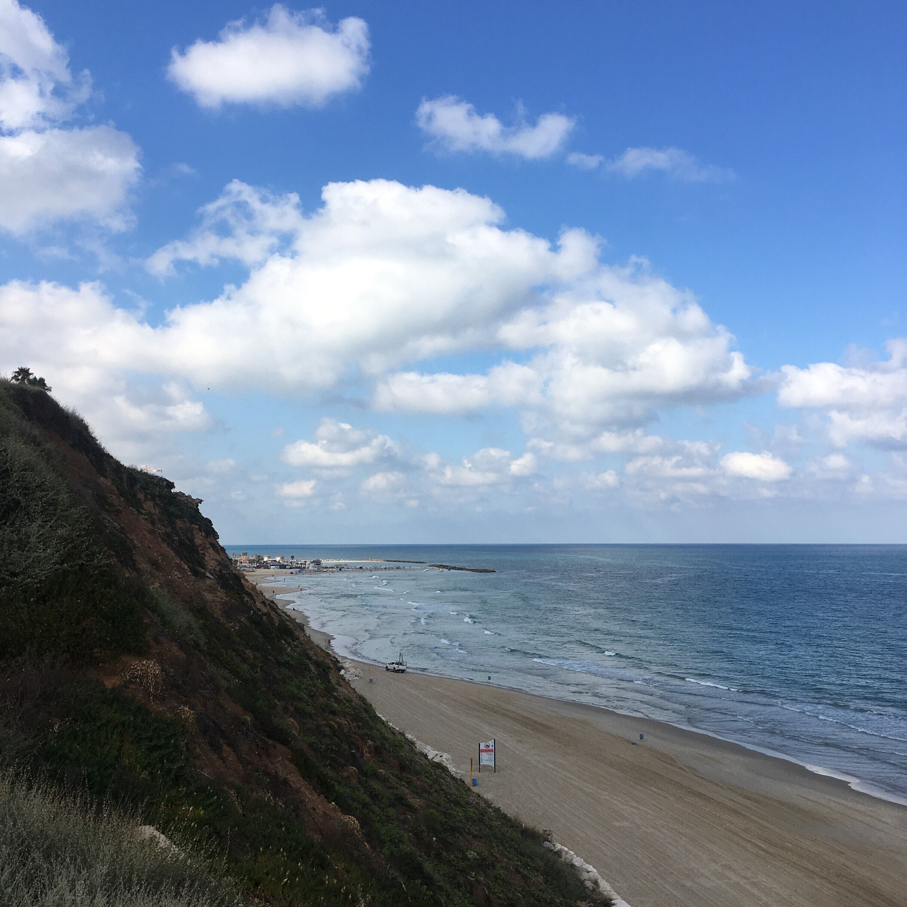 A coastal beach with a clear sky and a rocky cliff.
