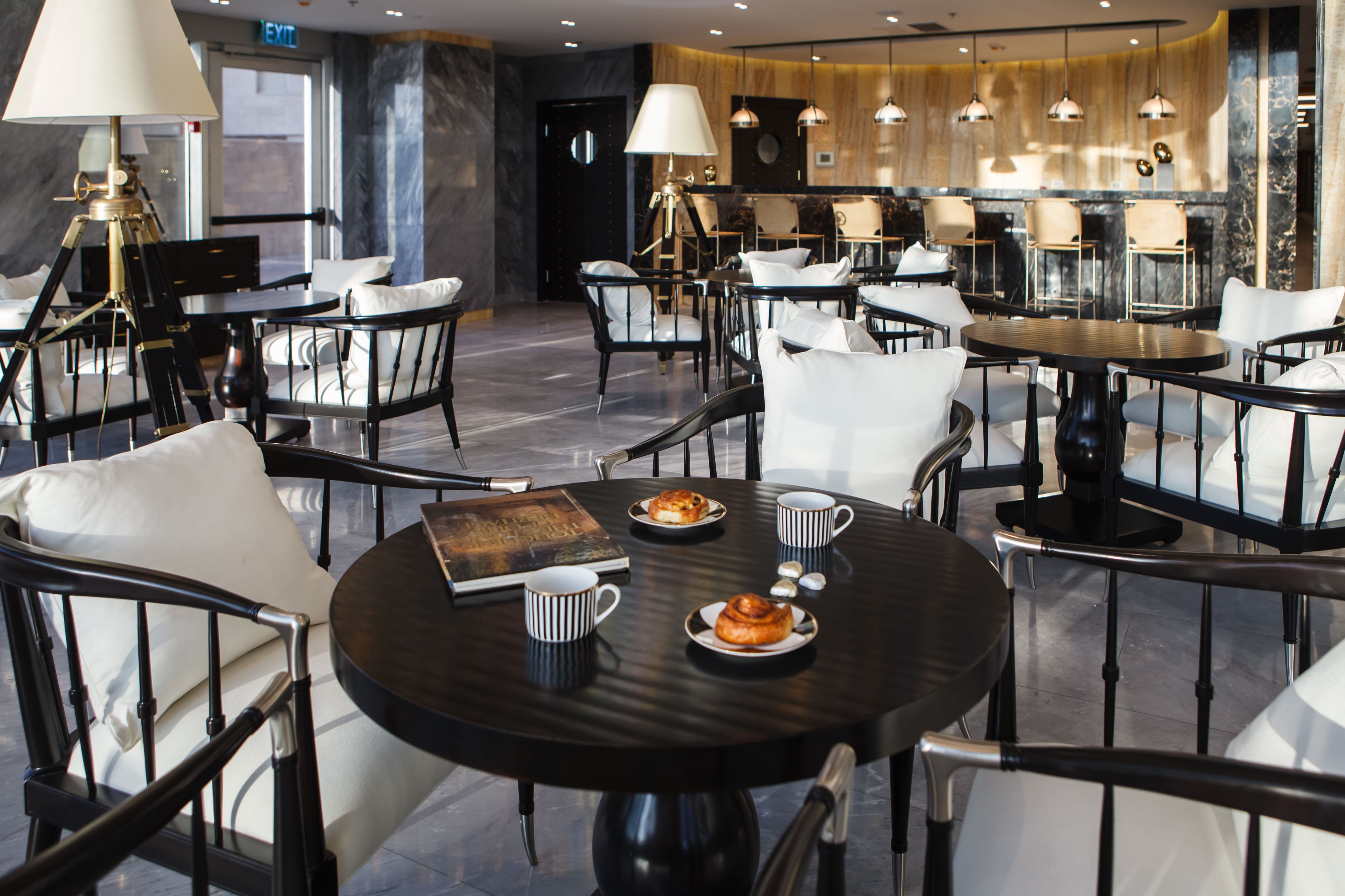 A modern dining area with round tables, white cushioned chairs, and a central chandelier.