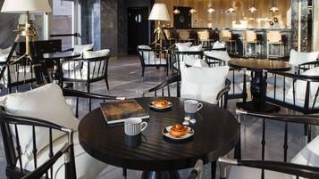 A modern dining area with round tables, white cushioned chairs, and a central chandelier.