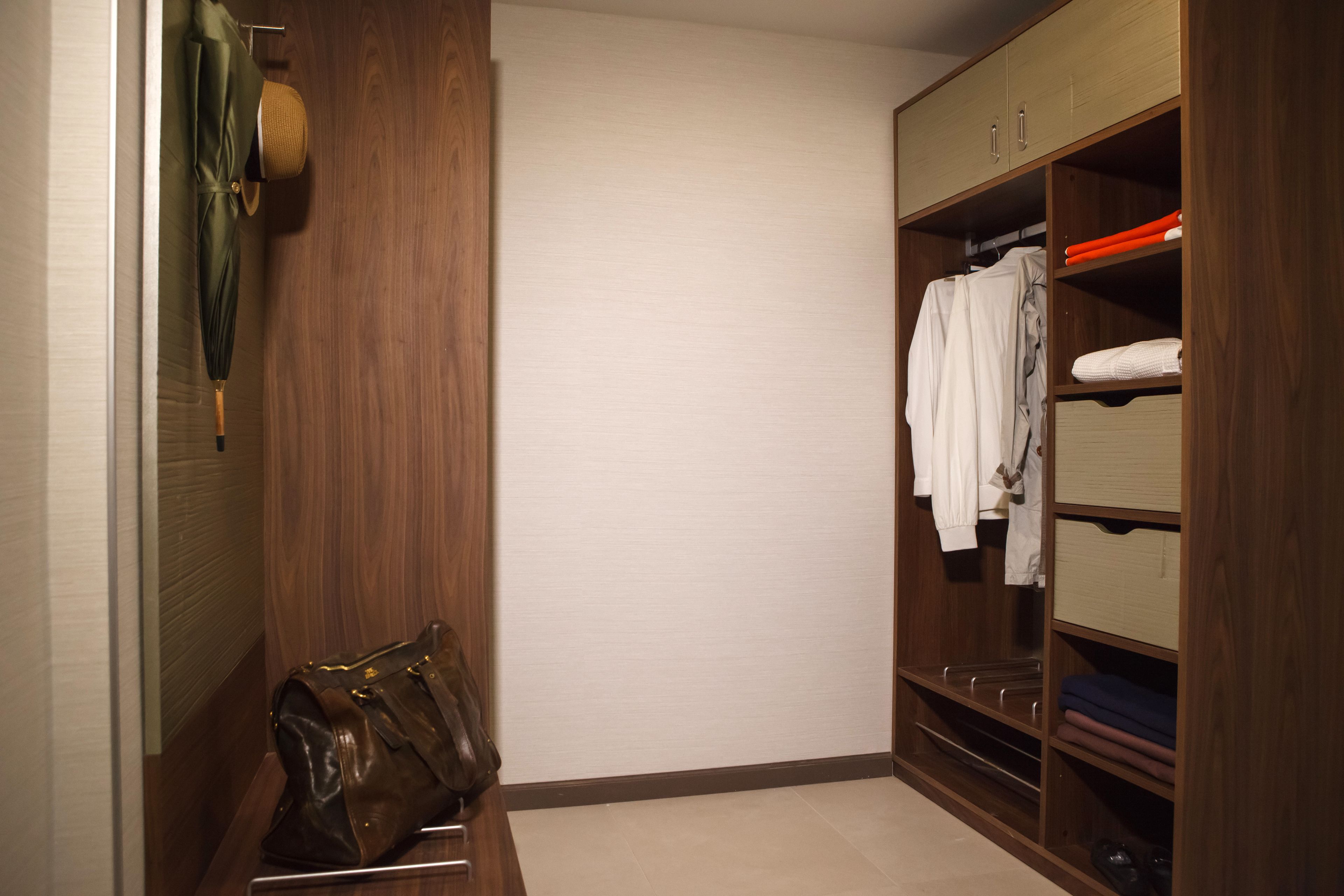 Ein begehbarer Kleiderschrank mit Holztüren, Regalen und Kleiderstangen.