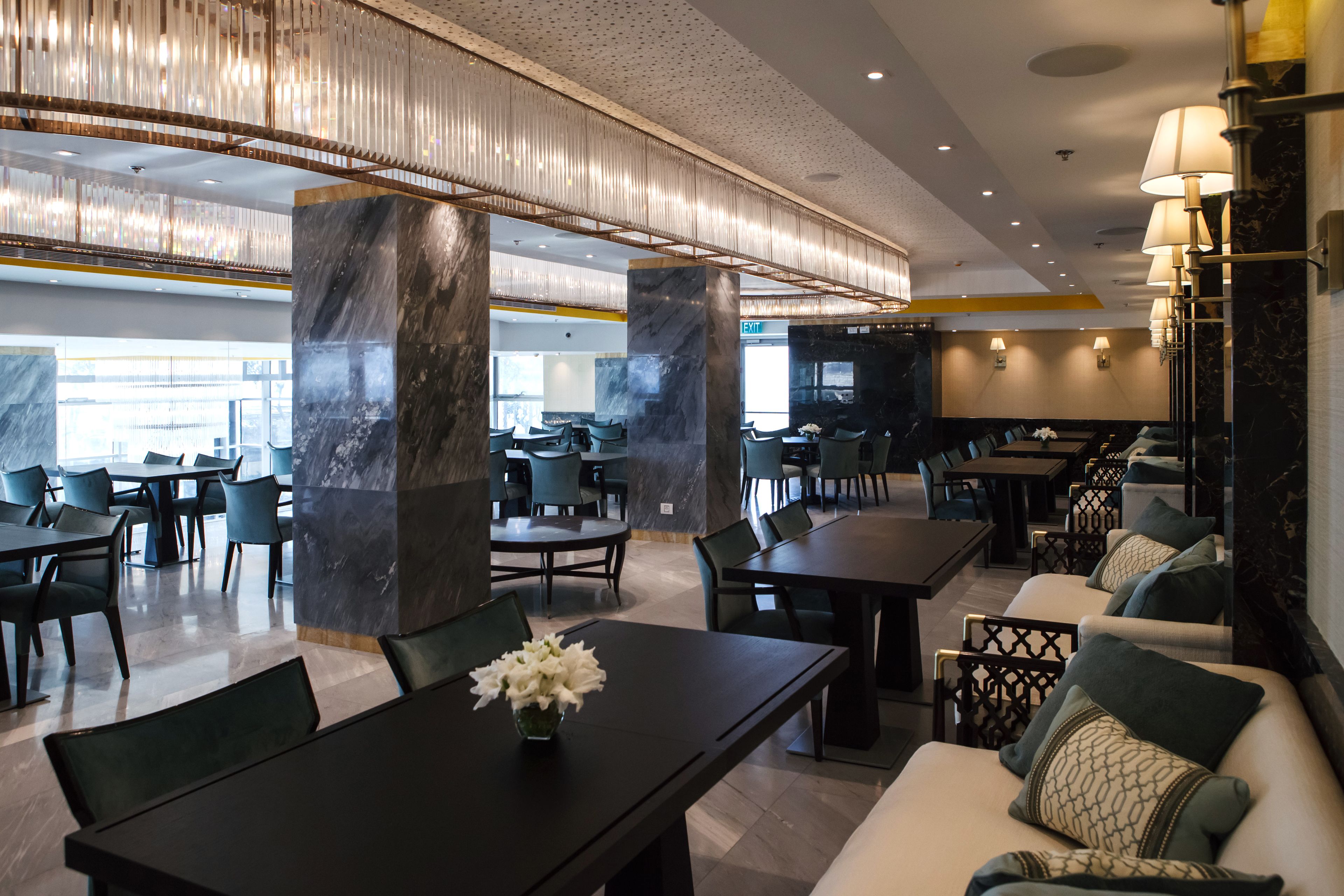 Un hall d’hôtel moderne, doté de colonnes en marbre, de tables à manger et d’espaces aménagés pour se détendre.