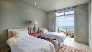 A hotel room with two beds, a nightstand, a lamp, and a view of the ocean. - 10 Elf Beach House (Glentana)