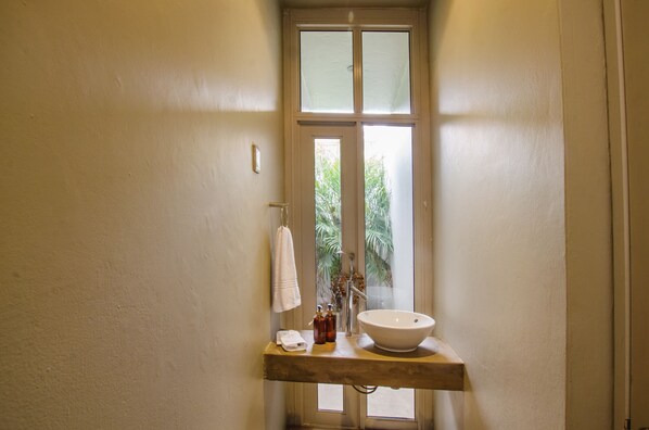 Un baño con un lavamanos blanco, una toalla colgada en la pared y una ventana con vistas a la vegetación.