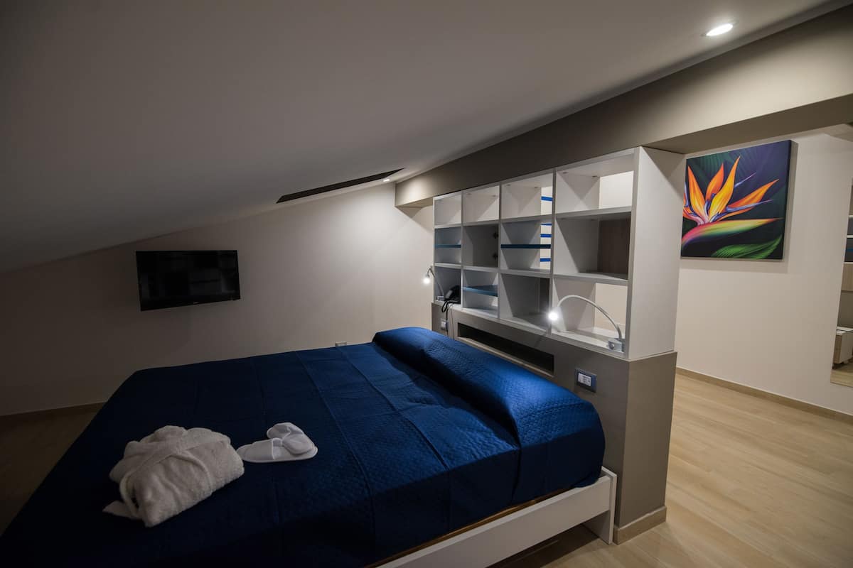 Ein Schlafzimmer mit einem Bett, einem an der Wand montierten Fernseher und einem Bücherregal.
