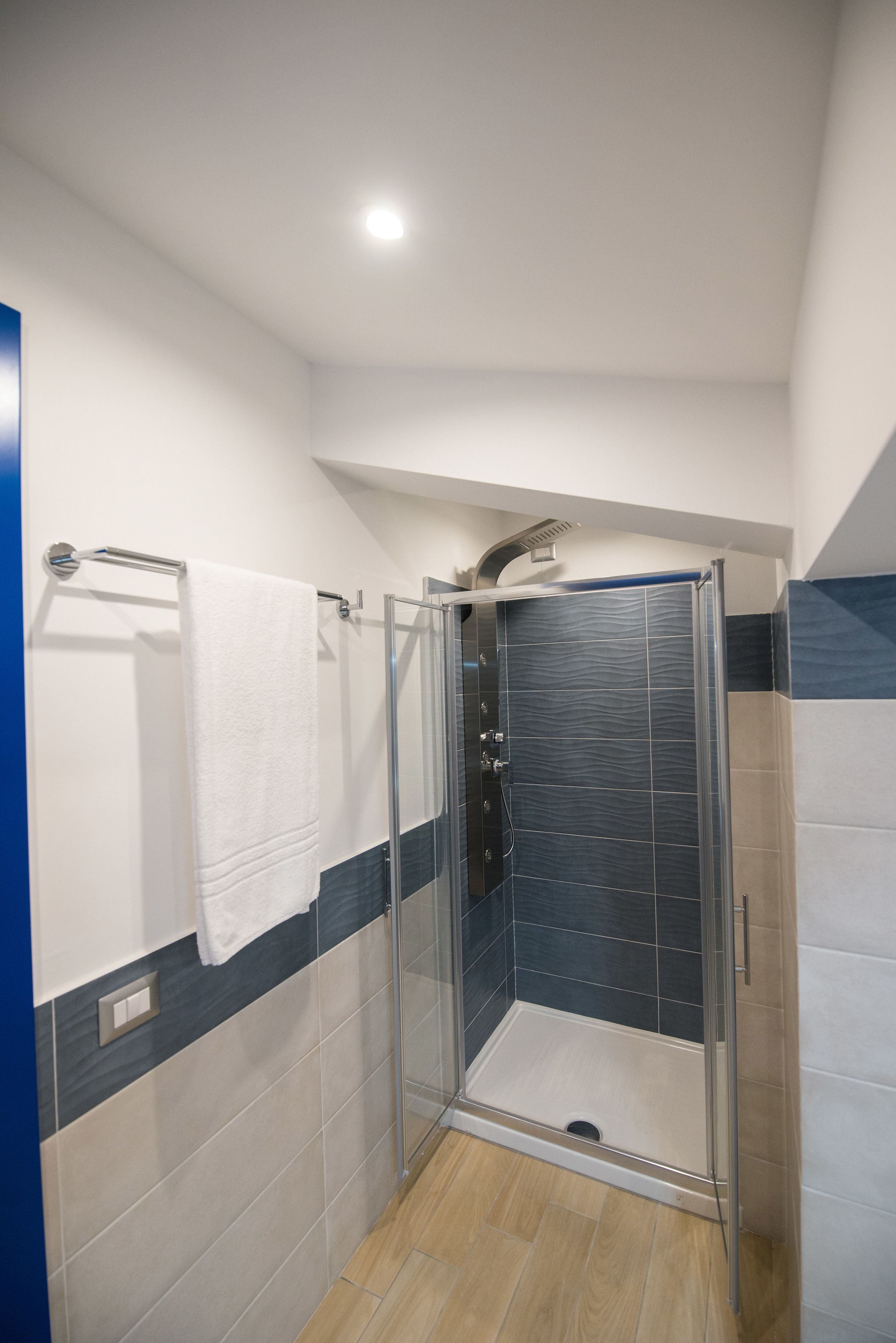 A modern shower area with a glass door, a towel rack with a white towel, and a combination of light and dark tiles on the walls.