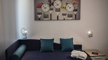 Een moderne slaapkamer met een donkerblauwe bed, kussens in teal en een wandklok met een bijzonder design.