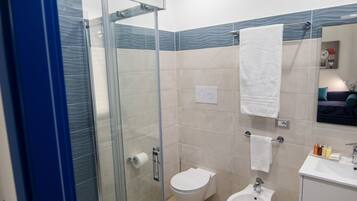 A modern bathroom with a glass shower enclosure, a toilet, a bidet, and a sink with a mirror above.