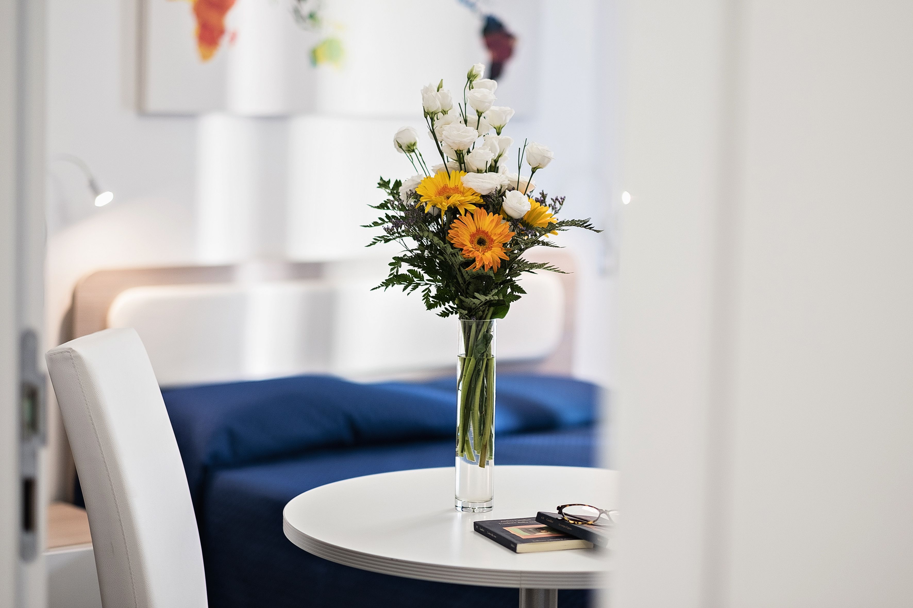 A round white table with a vase of flowers, a book, and a pair of glasses.