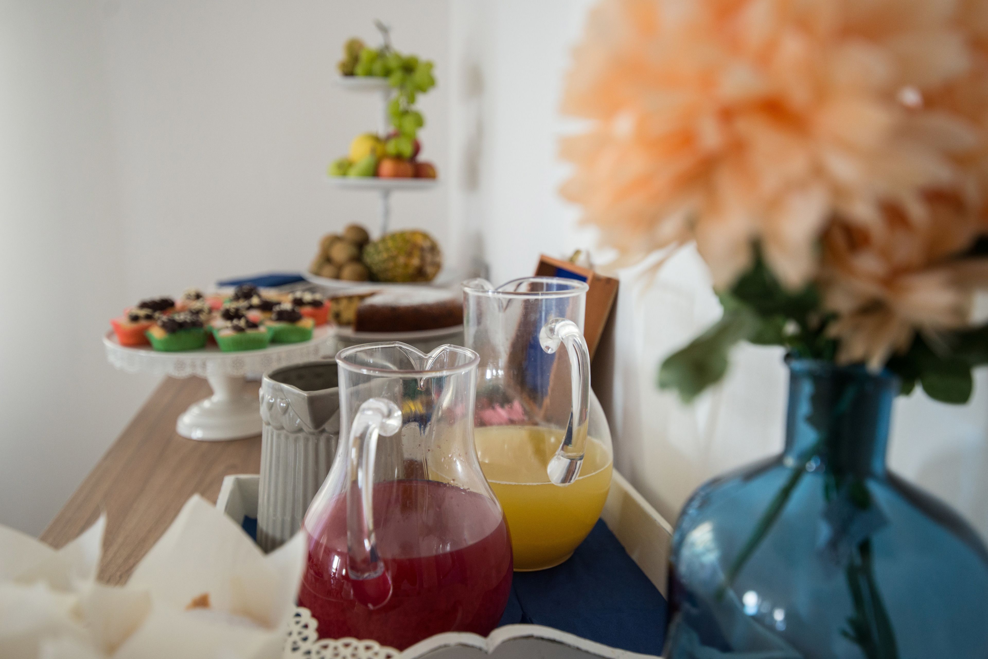 A table with a pitcher of red liquid, a yellow liquid, and a blue vase with flowers.