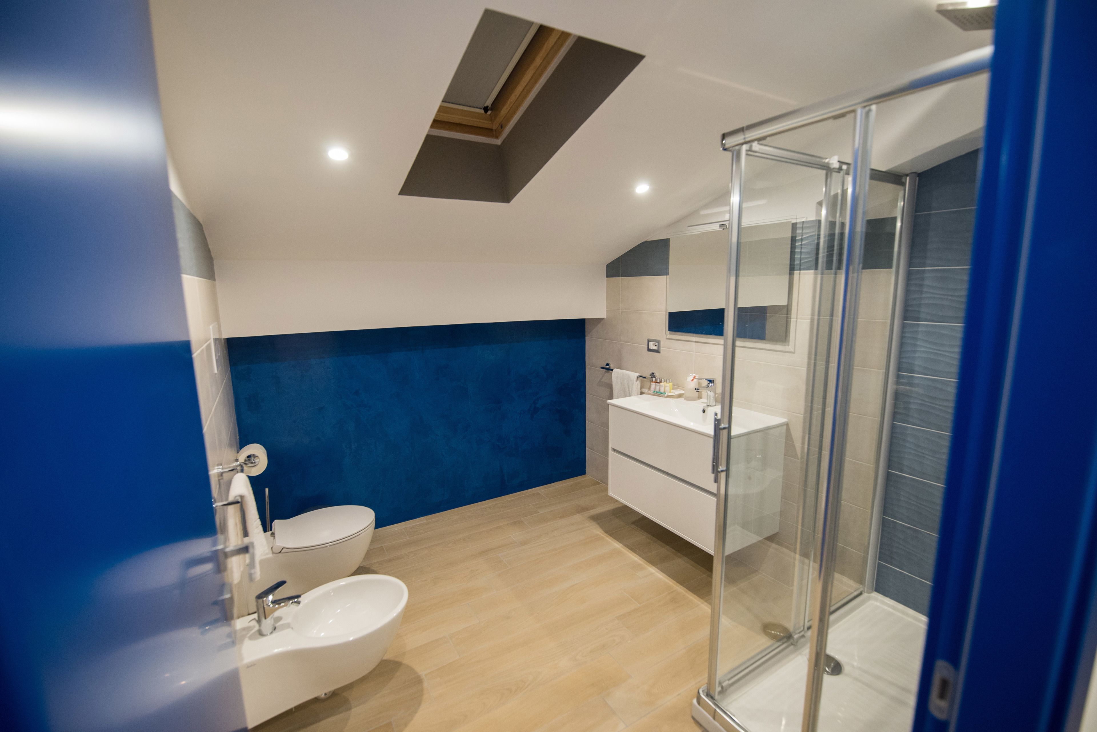 A modern bathroom with a skylight, a glass shower enclosure, and a white sink.