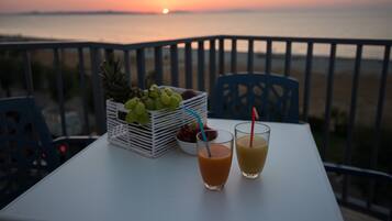 Un tavolo con due bevande e un cesto di frutta su un balcone affacciato sul mare al tramonto.