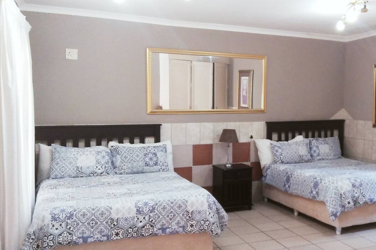 A bedroom with two beds, a bedside table, a lamp, a mirror, and a wall-mounted air conditioner.
