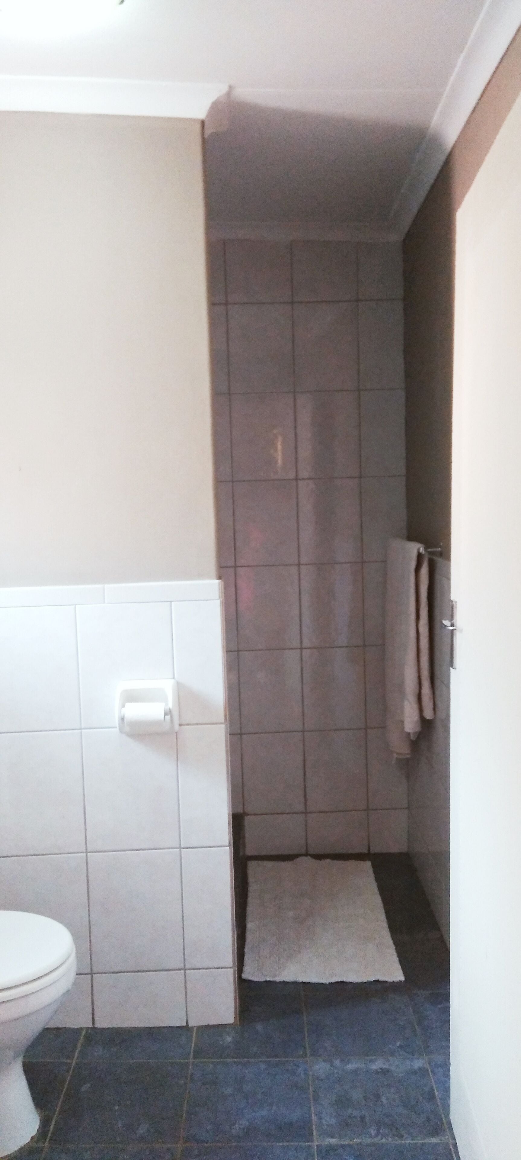 A bathroom with a toilet, a shower area with tiled walls, and a towel hanging on a rack.