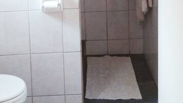 A bathroom with a toilet, a shower area with tiled walls, and a towel hanging on a rack.