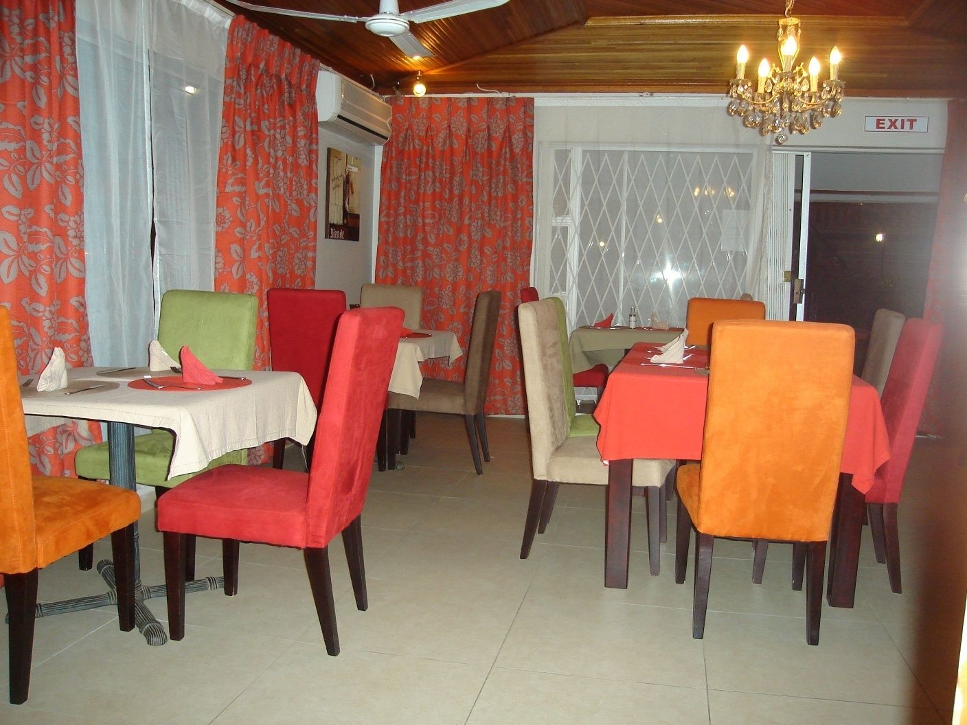 A dining area with multiple tables and chairs, some with red and orange upholstery.