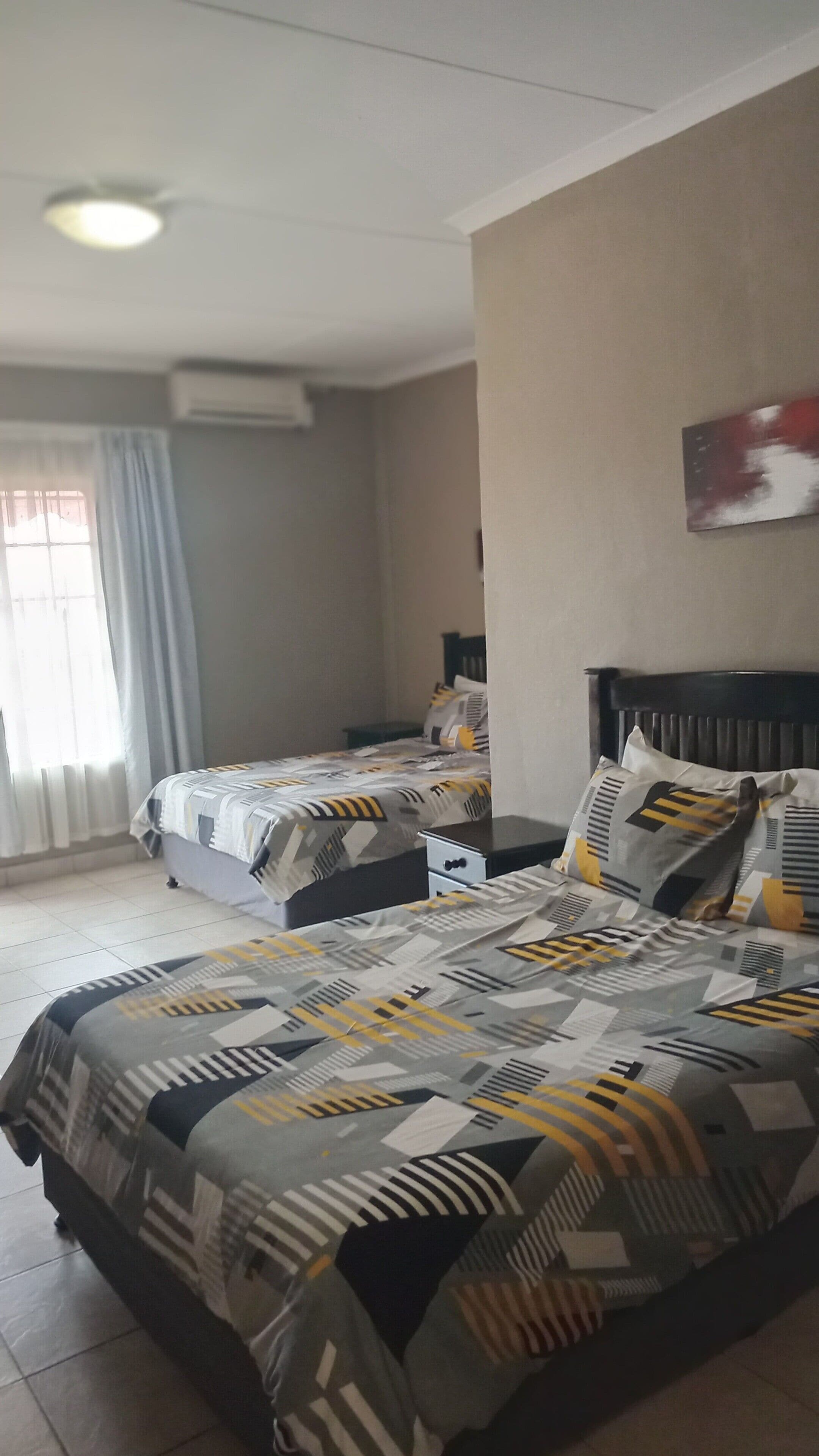 Une chambre d’hôtel avec deux lits, une fenêtre avec des rideaux, un luminaire au plafond et un climatiseur fixé au mur.