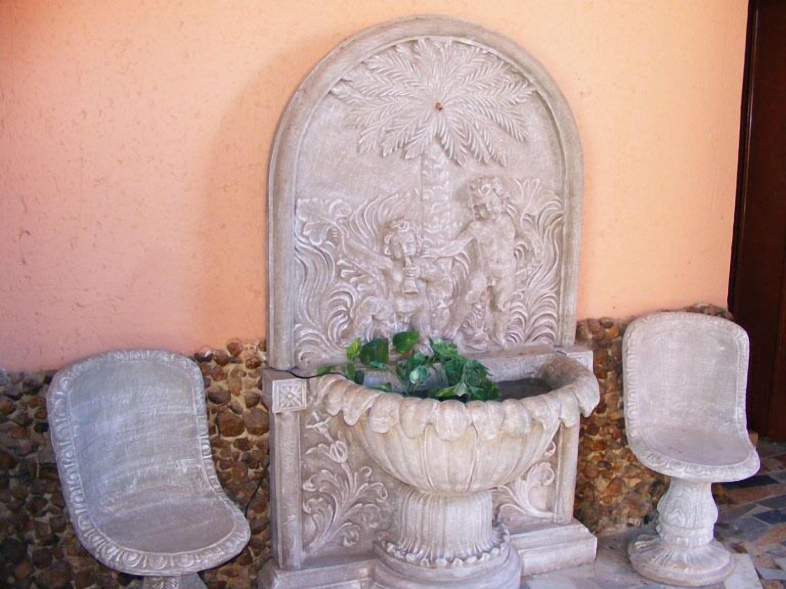 A stone fountain with intricate carvings, two stone benches, and a stone wall.