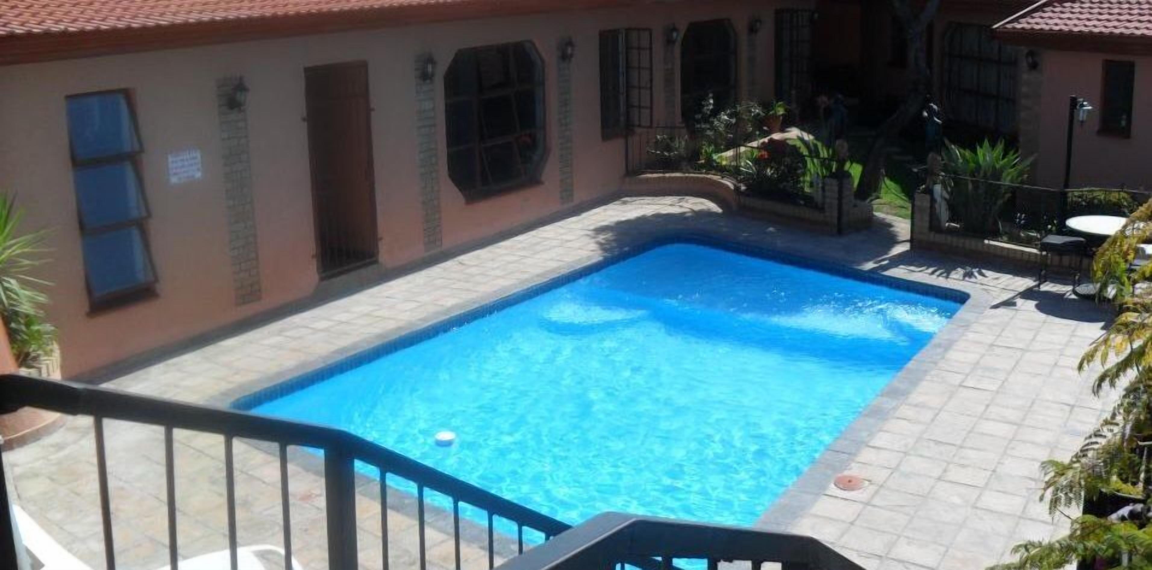 A swimming pool with a tiled deck, surrounded by a building with arched windows and a tiled roof.
