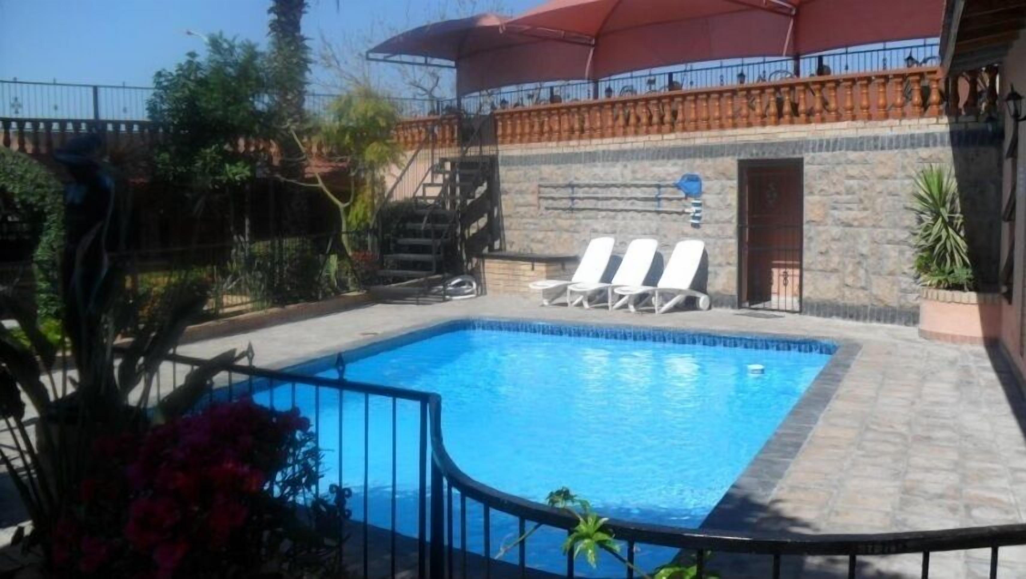 A swimming pool with two lounge chairs, surrounded by stone walls and a red umbrella.