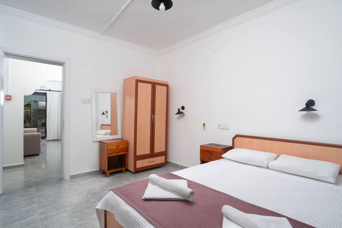 Un dormitorio con cama, armario, tocador con espejo, mesita de noche y lámpara de pared.