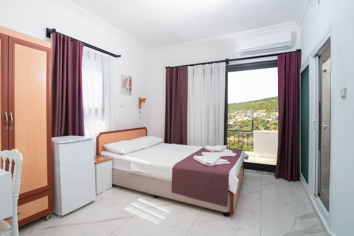 Una habitación de hotel con cama, escritorio, refrigerador y vista a una colina.