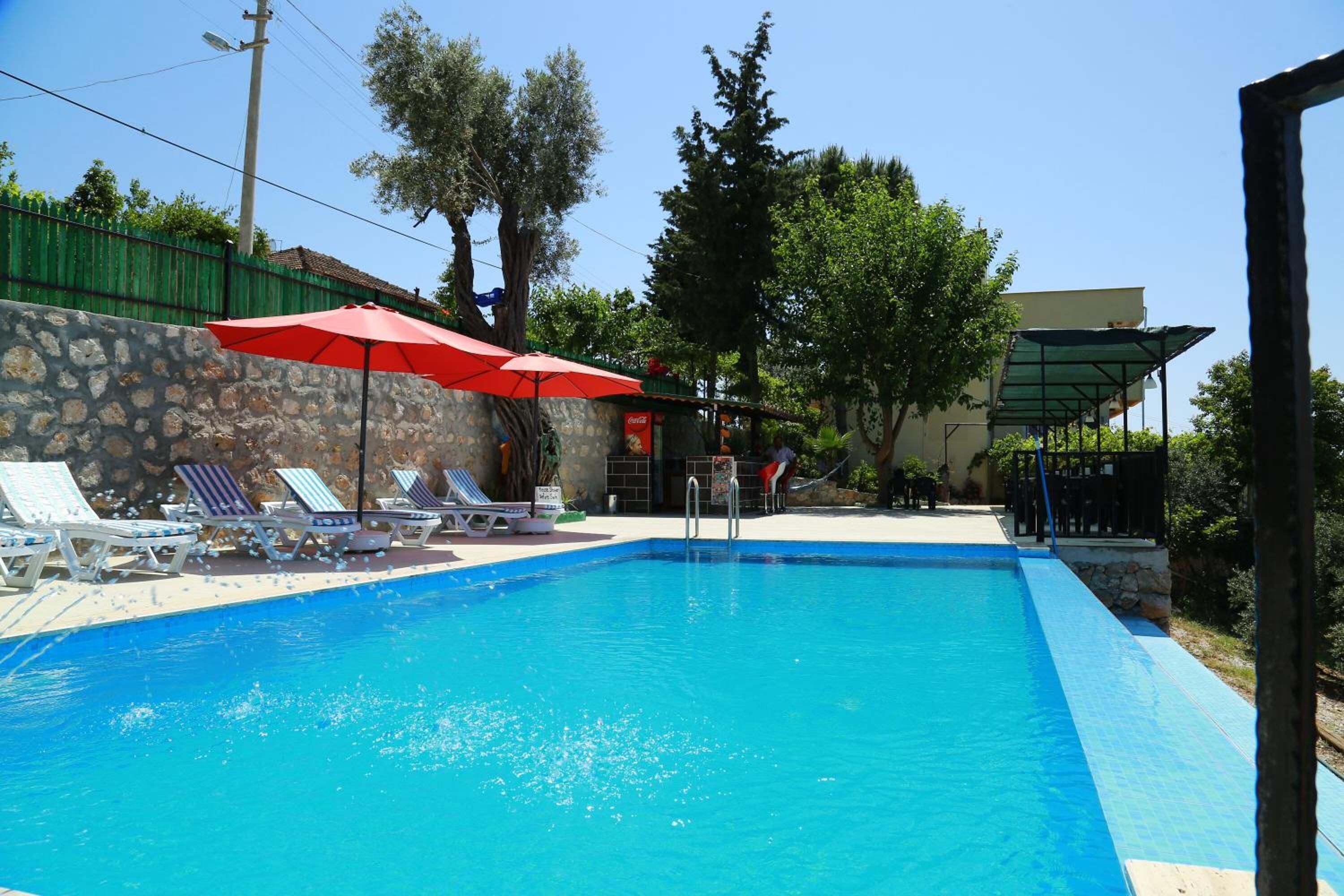 Una piscina con sillas de descanso y sombrillas, rodeada de muros de piedra y árboles.