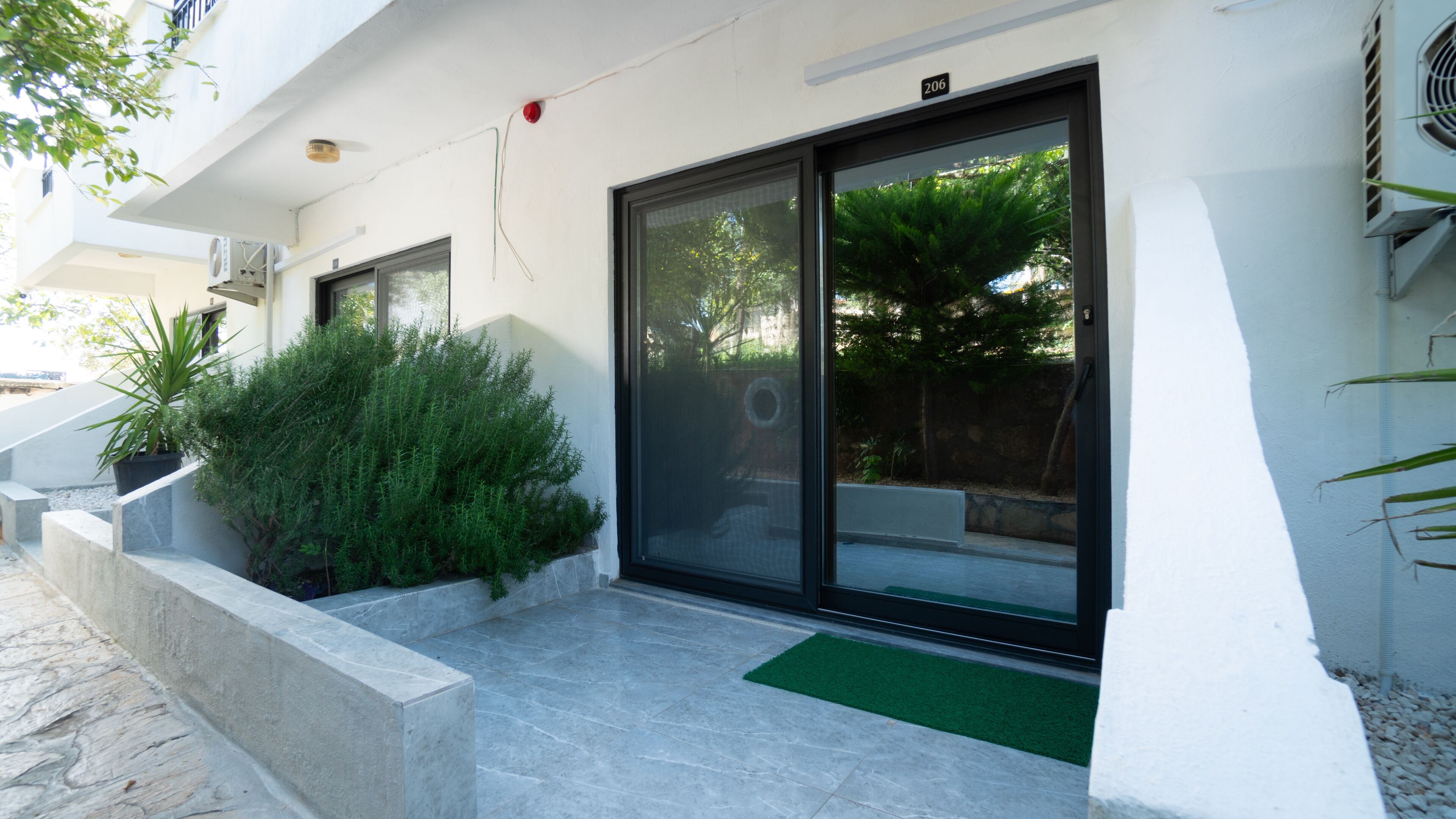 A modern building with a stone facade, large sliding glass doors, and a small green area with plants.