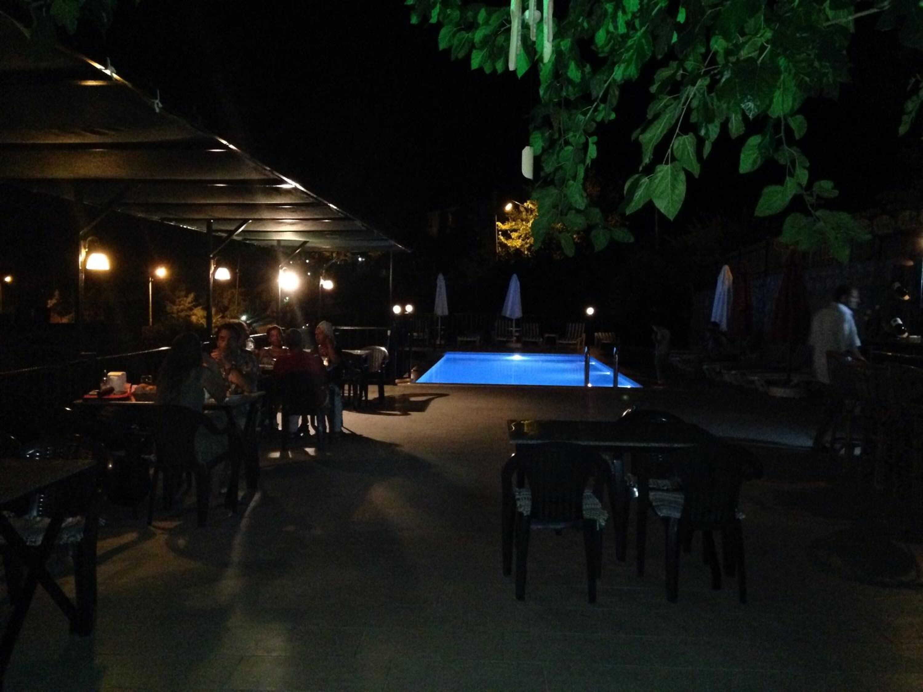 An outdoor dining area with tables and chairs, a pool, and umbrellas providing shade.